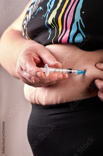 Woman with syringe make a subcutaneous abdomen injection of insulin to her belly
