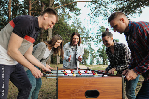 Friends play table football or kicker outdoors. Players and fans rejoice in the victory.