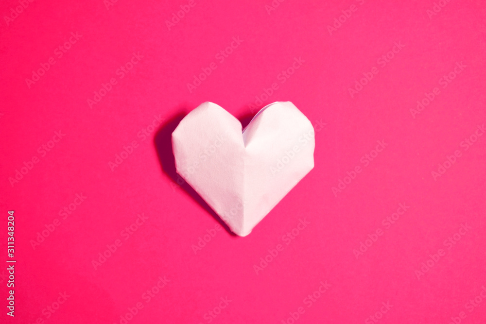 The Background Of Valentine's Day. One heart made of origami paper, in the center on a pink background. The Concept Of Valentine's Day. Flat lay. Top view, copy space.