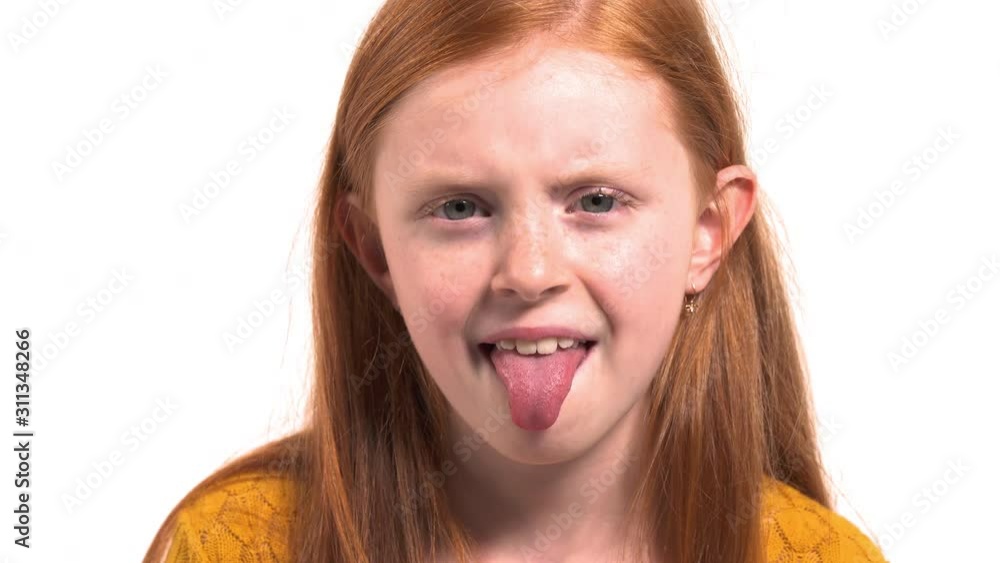 Funny little girl looking in camera showing tongue. Young model with beautiful foxy hair with freckles making grimaces and having fun Funny little girl looking in camera showing tongue. Young model with beautiful foxy hair with freckles making grimaces and having fun