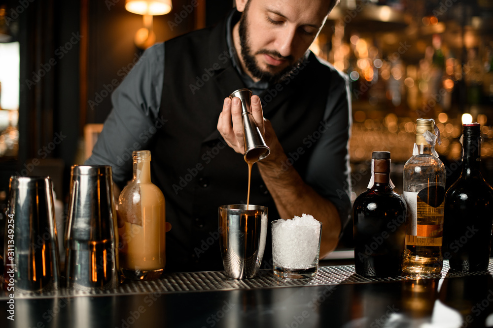Male bartender pouring a creamy liqour from the jigger to a steel shaker