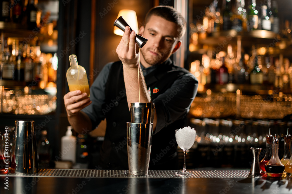 Male bartender pouring a liqour from the jigger to a professional steel shaker