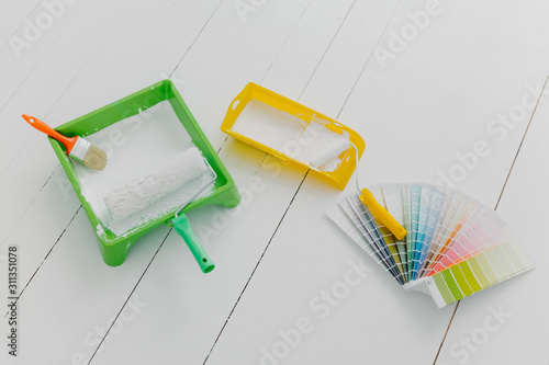 Top view of paint trays, brushes and rollers, color palette sample, white floor. Tools for making repairing and remodeling of house. Design concept photo