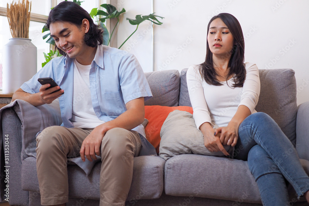The wife is suspicious of the husband while the husband is sitting on the phone. The wife is suspicious of the husband while the husband is sitting on the phone.