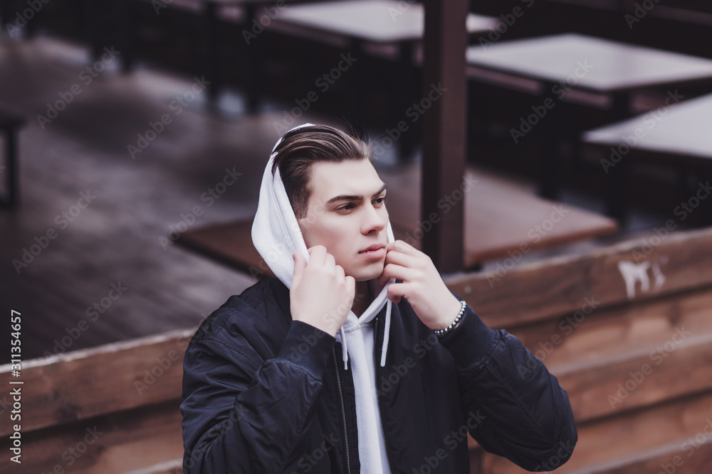 Fototapeta premium portrait of a handsome man in a black jacket and hood in an urban environment