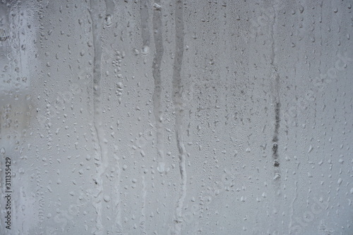 Frozen drops of water on a transparent glass surface on a gray background.