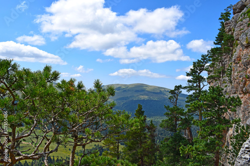 Picturesque mountains, meadows, green pines on the cliff side. Blue sky and white clouds. Summer landscape, sunny day. Horizontal photo. Lago-Naki Plateau, Adygea.
