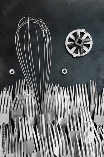 Whisk for whipping lies on an old wall in the middle of a sea of ​​forks. The design idea has transformed the subject of making it wonderful, fanastastic as from wonderland. Revived subject with eyes.