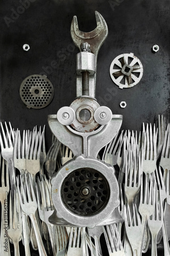 Old meat grinder lies on an old wall in the middle of a sea of ​​forks. The design idea has transformed the subject of making it wonderful, fanastastic as from wonderland. A revived subject with eyes.