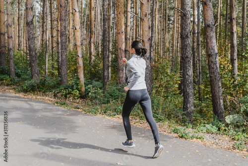 Runner athlete running on a forest trail. woman fitness running workout Wellness concept. girl on a run in the woods. A young fitness athlete runs along the Park trail