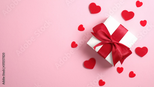 Happy Valentine's Day banner. White gift box with red ribbon bow and red hearts on pink background. Flat lay, top view, overhead. © photoguns