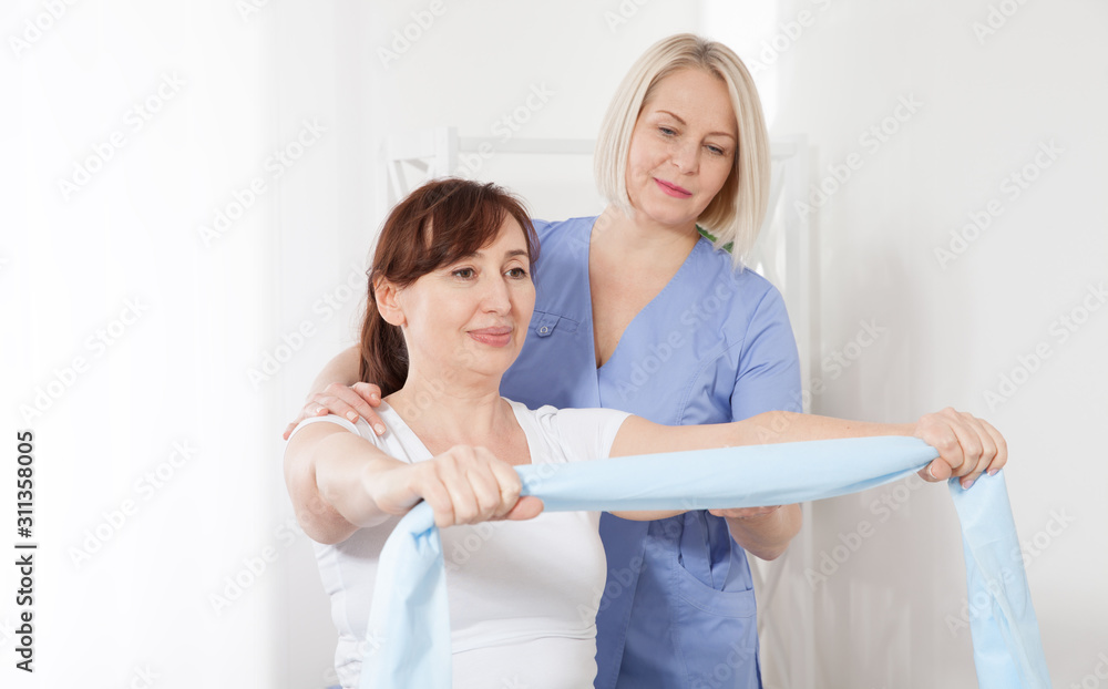 Fototapeta premium Physiotherapist and woman sitting on a bed exercising with a rubber tape