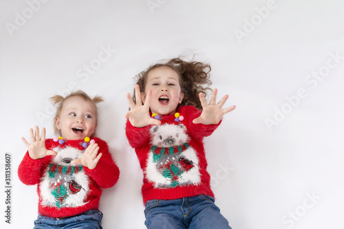 Two little girls-sisters in red sweaters-koala and blue jeans, on a white background. The view from the top. The concept of a happy childhood. Blank space for text. Layout for design