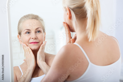 Middle aged woman looking at wrinkles in mirror. Plastic surgery and collagen injections. Makeup. Macro face. Selective focus