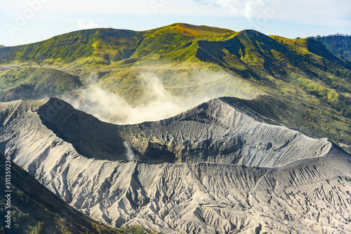 Close-up view of the Mount Bromo crater in the foreground and green hills in the distance during a beautiful sunset. Mount Bromo is an active volcano in East Java, Indonesia. photo