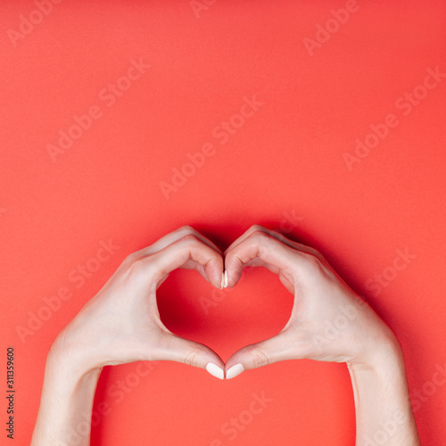 Female hands show a heart symbol on a red background. Place for text.