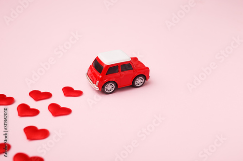 Red retro toy red car with red bow for Valentine's day on pink background with heart confetti