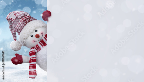 Fotografia Happy snowman in the winter scenery behind the blank advertising banner with cop