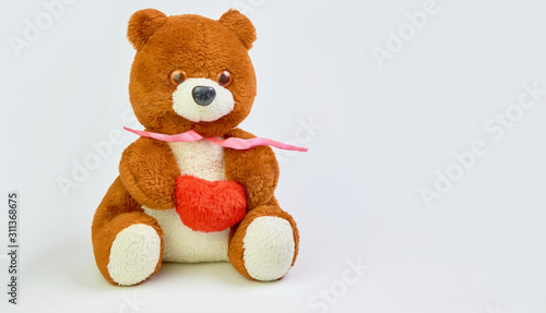 Teddy bear with a red heart in hands on a light background with place for text.