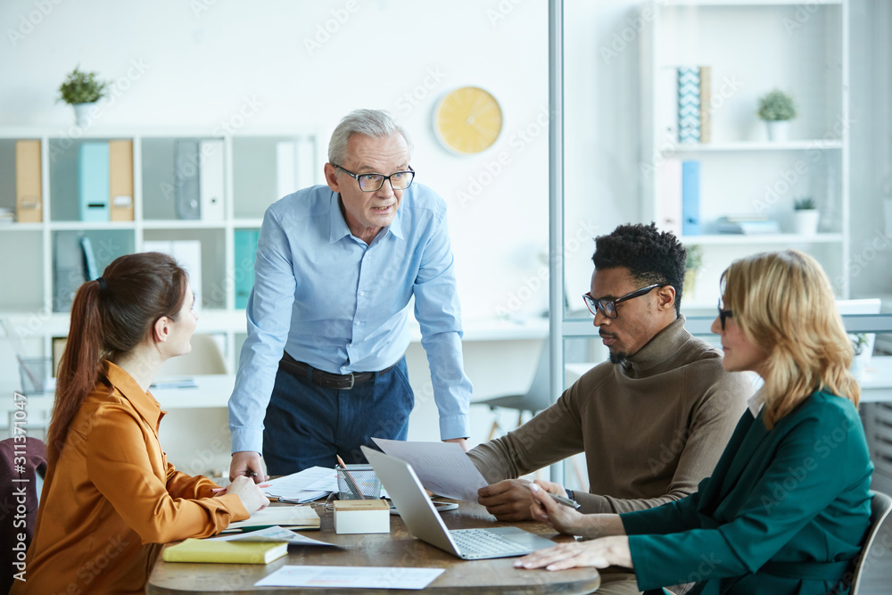 Fototapeta premium Multiethnic business people sitting at the table and listening to mature businessman during business meeting at board room