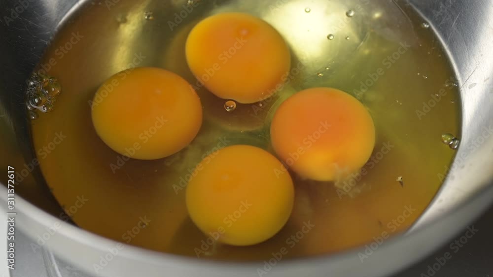 Adding raw chicken eggs to a metal bowl. Adding raw chicken eggs to a metal bowl.