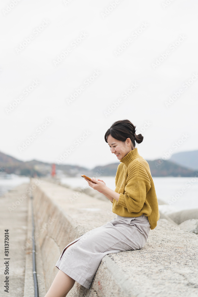 海でスマートフォンを使う女性