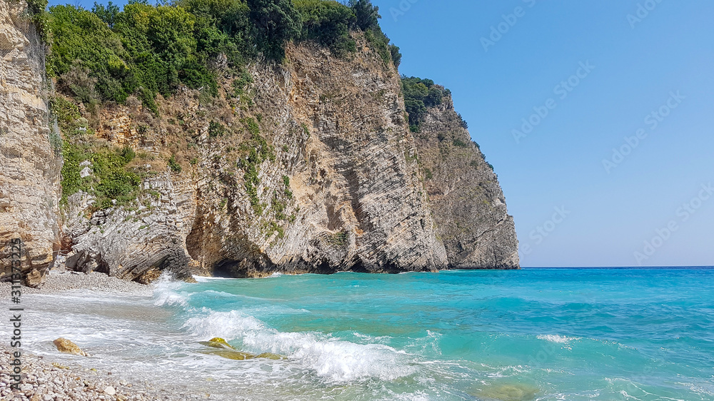 Panoramic view of pebble beach with clear azure blue water and layered rocks, beautiful mediterranean Adriatic Sea coast, Montenegro, selective focus Panoramic view of pebble beach with clear azure blue water and layered rocks, beautiful mediterranean Adriatic Sea coast, Montenegro, selective focus