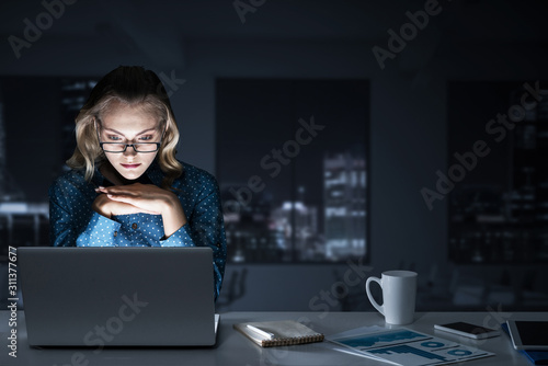Obraz na płótnie Attractive blonde working on laptop in dark office. Mixed media w salonie