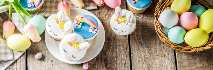 Easter holiday greeting card background. Cute homemade cupcakes with traditional Easter bunny, egg and springtime flowers decor. Happy easter concept. Copy space for your text