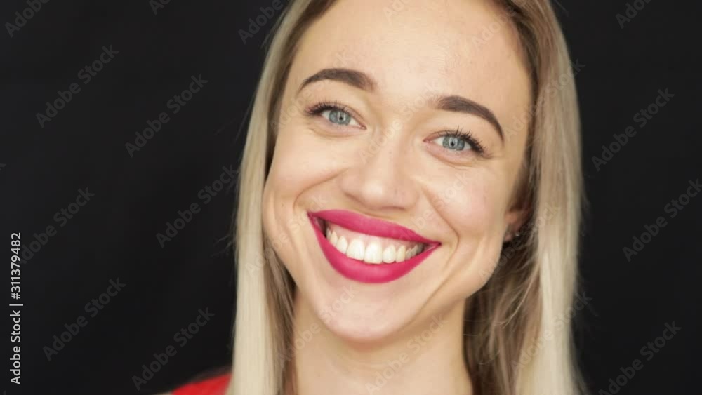 beautiful wide smile of blonde woman with big red lips and blue eyes. Looking friendly and with love. Black background. Video footage. Close up portrait beautiful wide smile of blonde woman with big red lips and blue eyes. Looking friendly and with love. Black background. Video footage. Close up portrait