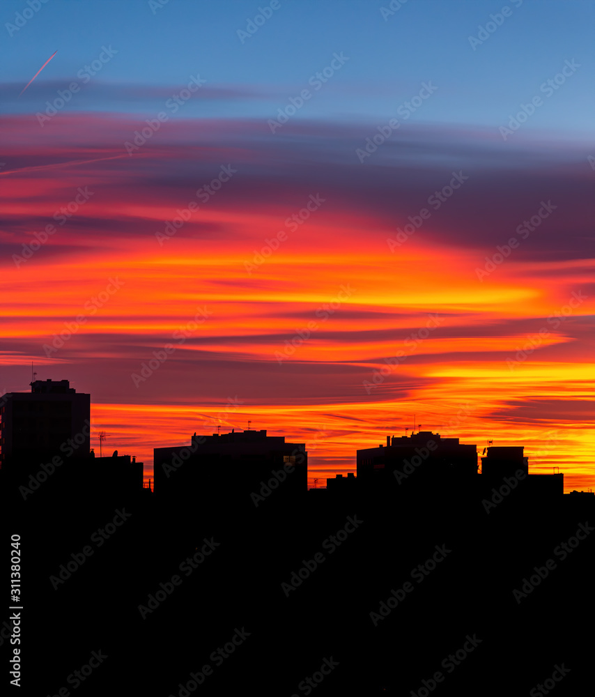 Amazing sunset with orange, pink and red stratus clouds over the city. Background for forecast and meteorology concept. Barcelona, Spain.
