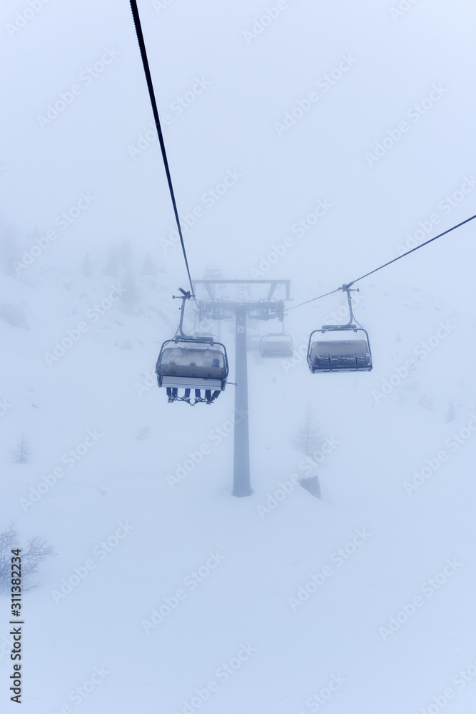 Frozen ski lifts covered with snow in misty weather and foggy day. Hard winter conditions, snowfall and fog. Dolomites, Italy, Europe. Frozen ski lifts covered with snow in misty weather and foggy day. Hard winter conditions, snowfall and fog. Dolomites, Italy, Europe.