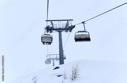 Frozen ski lifts covered with snow in misty weather and foggy day. Hard winter conditions, snowfall and fog. Dolomites, Italy, Europe.