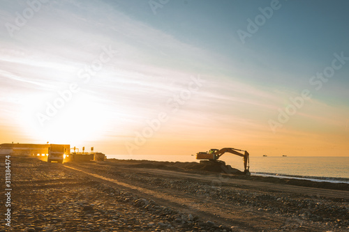 Excavator loads the excavation onto a truck (hydraulic)are heavy construction equipment consisting of an arrow,a bucket and a cabin on a rotating platform.On the beach with the sea and the setting sun