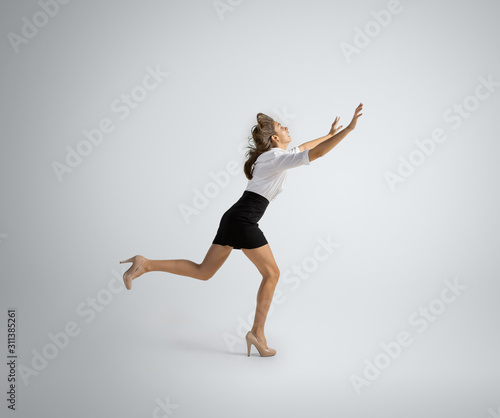 Hurrying up to new goals. Woman in office clothes running on grey studio background. Businesswoman training in motion, action. Unusual look for sport, new activity. Sport, healthy lifestyle.