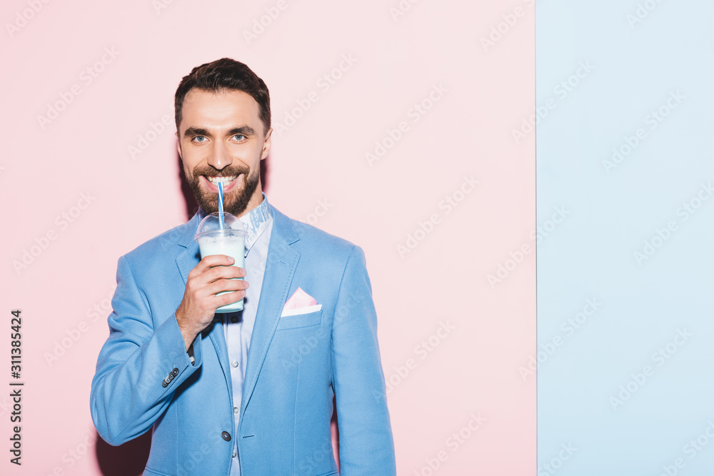 smiling man drinking cocktail on pink and blue background smiling man drinking cocktail on pink and blue background