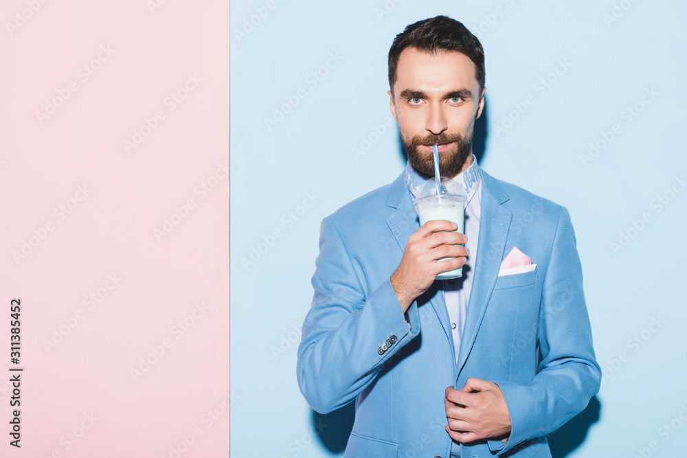handsome man drinking cocktail on pink and blue background