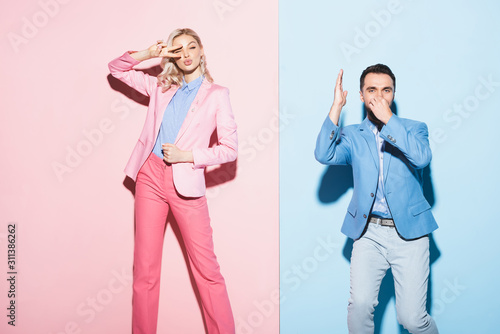 attractive woman showing peace gesture and handsome man showing dive gesture on pink and blue background