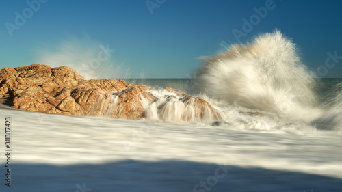 The waves breaking on a stony beach, forming a spray.