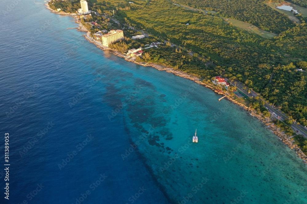 Coast line of Cozumel island with catamaran on turquoise blue ocean, beach front hotels and tropical forest