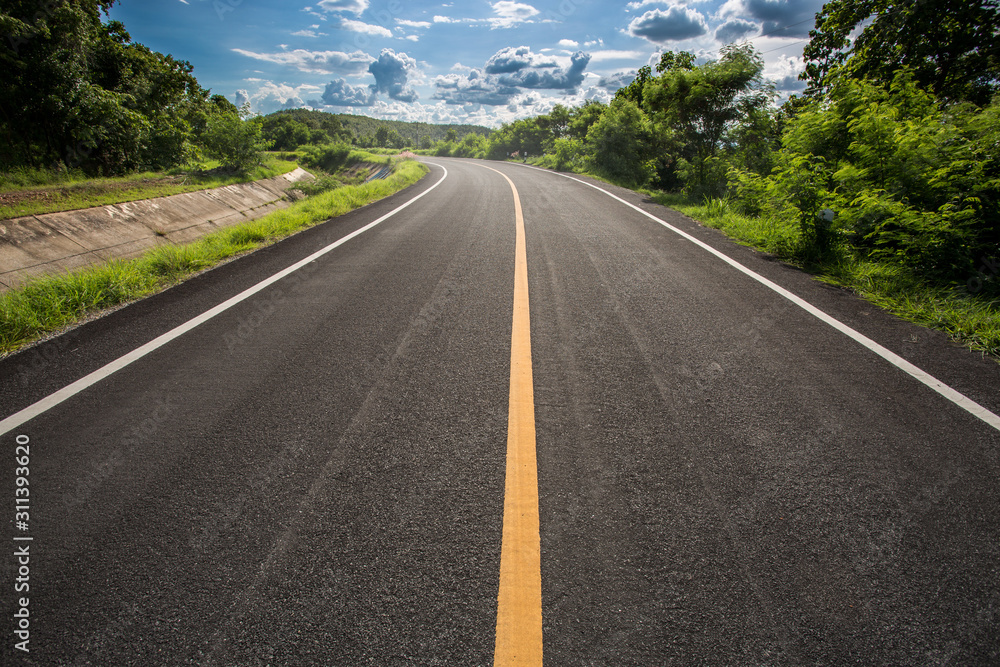 Asphalt road through the green field and clouds on blue sky in summer day. Beautiful grassland road in Thailand.Highland road.