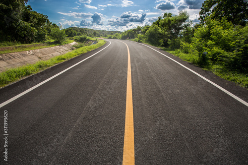 Asphalt road through the green field and clouds on blue sky in summer day. Beautiful grassland road in Thailand.Highland road.