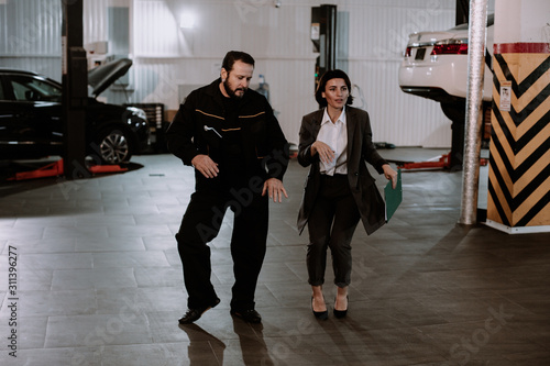 Good looking manager woman in a suit and the mechanic man attractive look dancing in a garage after they finished the work day