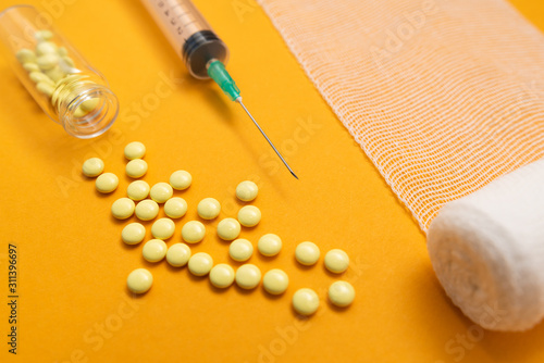 Syringe with pills for injection and vaccination on yellow background with bandage, concept of medecine