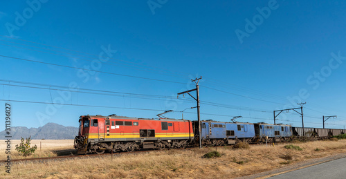 Hermon, South Africa. December 2019. Freight trains hauling wagons through countryside with a mountains backdrop.