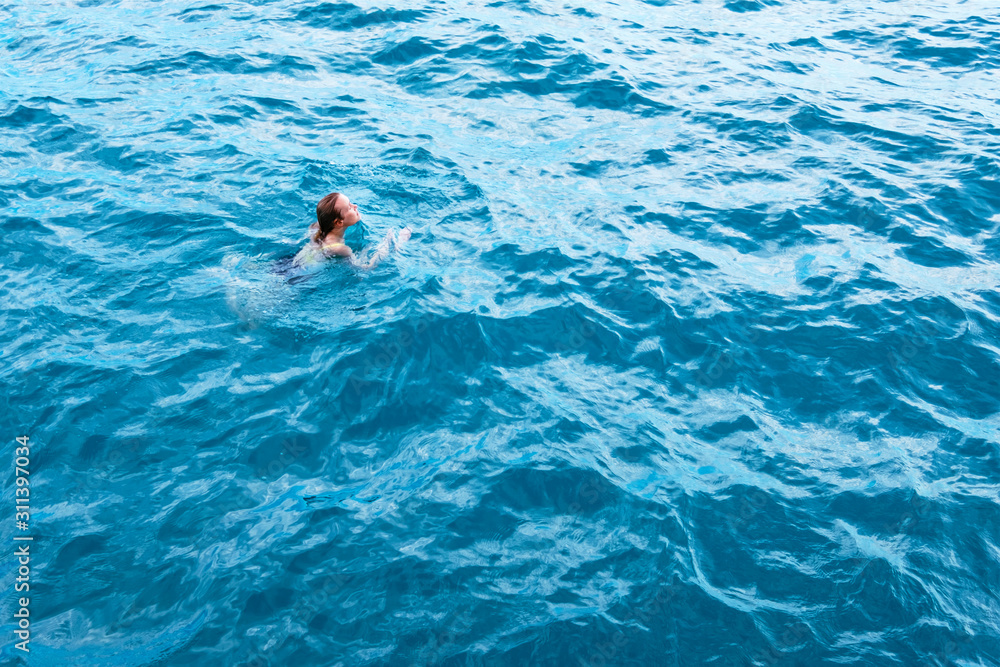 Young woman in blue water, aerial view. Sexy girl relaxing in sea captured from drone. Tropical summer vacation. Tranquility and peace. Person floating on back in ocean. Stock photography.