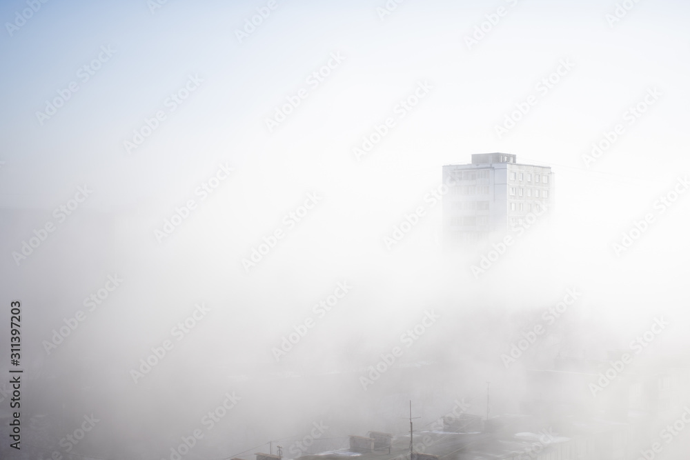 Fototapeta premium White clouds of fog envelop buildings at residential district. Urban panorama