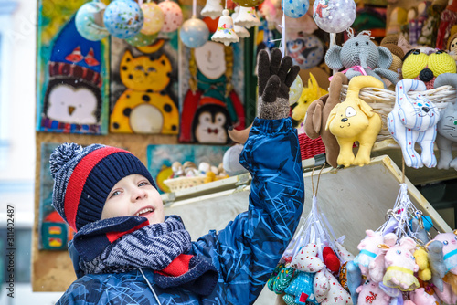 Little cute kid boy selecting decoration on Christmas market. Beautiful child shopping for toys and decorative ornaments. Traditional winter holiday event