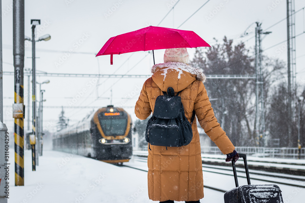 Woman with umbrella and luggage looking to arriving train during snowing Woman with umbrella and luggage looking to arriving train during snowing