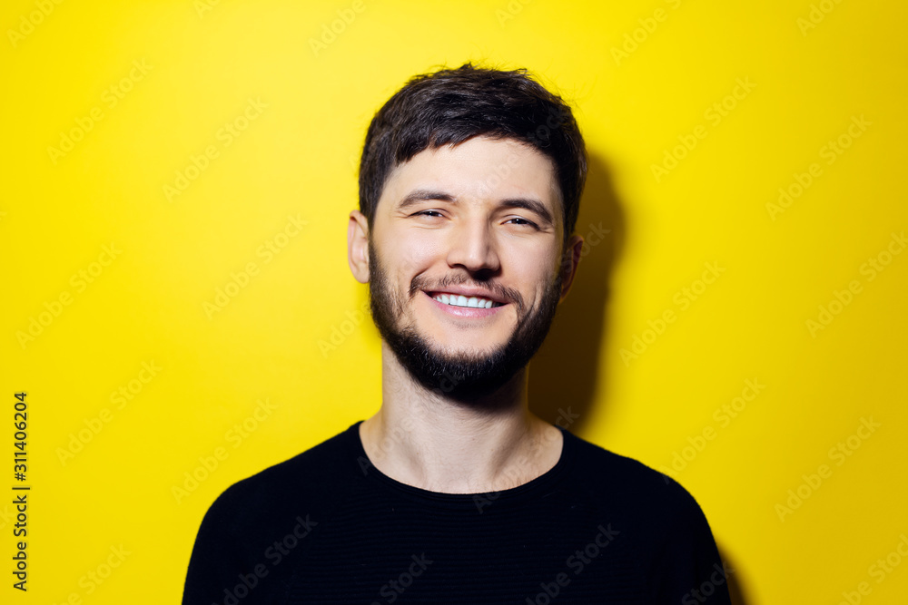 Fototapeta premium Studio portrait of young smiling man wearing black on yellow background.